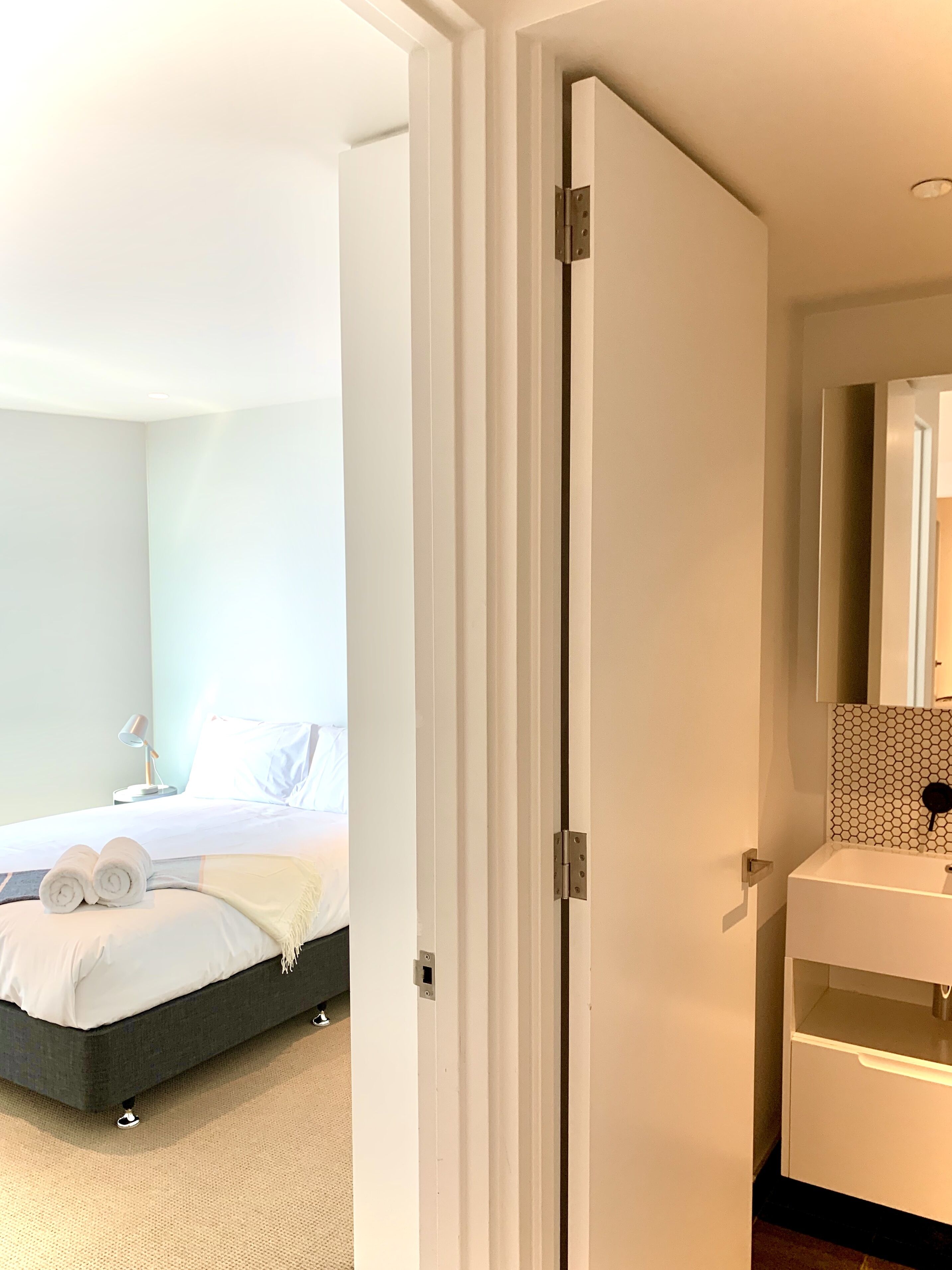 Et hotelværelse med seng, natbord, toiletbord, spejl og badeværelse med vask og toilet.