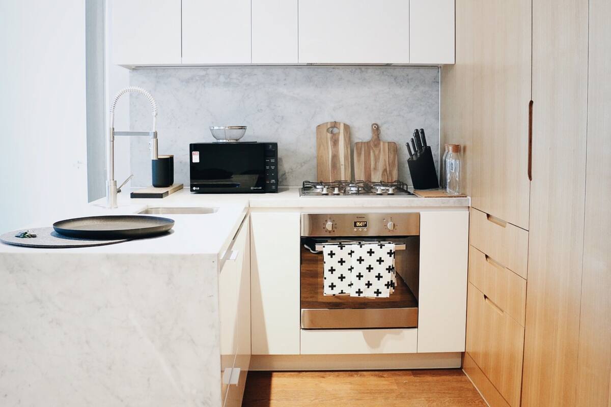 Una cocina compacta con armarios blancos, microondas integrado, estufa a gas y horno de acero inoxidable.