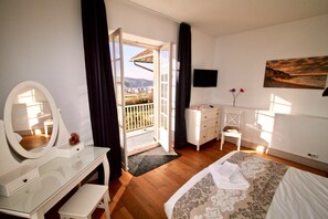 Une chambre à coucher comprenant un lit, une commode, un miroir, une télévision et un balcon avec vue.