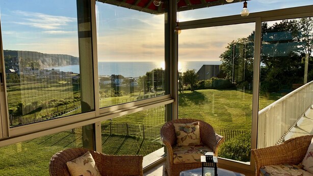 A room with large windows offering a view of a grassy area and distant buildings. There are wicker chairs and a small table with a lantern. - Grand Duplex ****, Sea View, 5 bedrooms, linen provided, private garden  (Hautot-Sur-Mer)