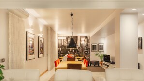 A modern living room with a dining area, featuring a large dining table, white sofas, and a hanging light fixture. - Porto RiverView Flat (Vila Nova de Gaia)