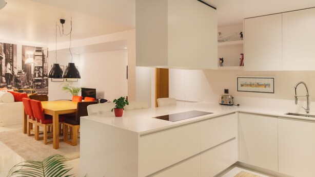 A modern kitchen with white cabinets, a central island, and a dining area with a wooden table and red chairs. - Porto RiverView Flat (Vila Nova de Gaia)