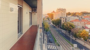 A balcony with a tiled wall and a red floor, overlooking a city street with trees and buildings. - Porto RiverView Flat (Vila Nova de Gaia)