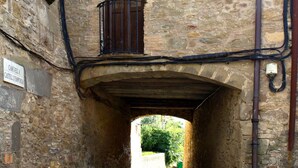 A narrow stone passageway with a wooden balcony and a sign indicating a castle entrance. - CASA CARINA (Ullastret)