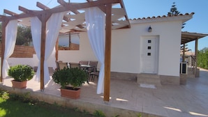 Un espacio de patio techado con una pérgola, plantas en macetas y mobiliario exterior.