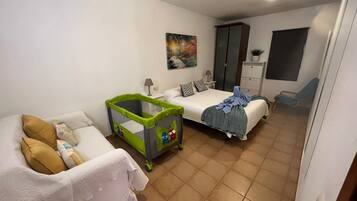 Cozy retreat with a neatly made bed, baby playpen, and comfortable sofa.