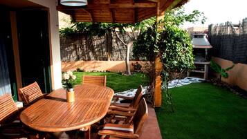 A wooden patio with a round table and chairs, a potted plant, and a thatched roof structure.