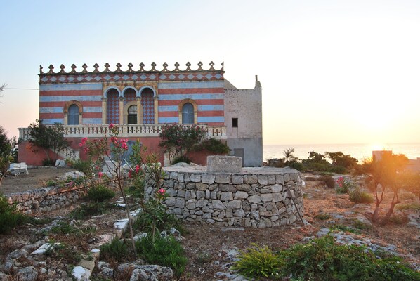 A building with a striped facade, arched windows, and a stone wall in the foreground. - Studio 2 / 4pl in Racale 4km from the sea (Racale)