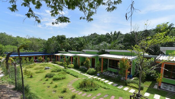 Un hotel con varios edificios con techos verdes, un jardín bien cuidado con senderos de piedra y abundante vegetación en el fondo.