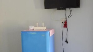 Una habitación con un refrigerador azul, un televisor montado en la pared y un bote de basura morado.