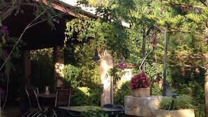 Ein Terrassenbereich im Freien mit Tisch und Stühlen, umgeben von Kübelpflanzen und einer Pergola.