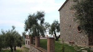 A stone building with a brick wall and metal gate, surrounded by trees and a grassy area. - POGGIO TAKUNA swimming among the olive trees... and more! !!  (Itri)