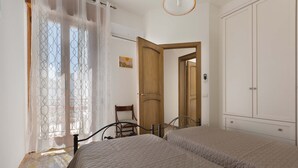 A bedroom with two beds, a wooden door, a chair, and a painting on the wall. - Appartamento Orizzonte by BarbarHouse (Porto Cesareo)