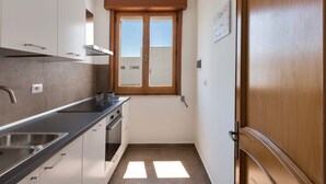 A compact kitchen with a window, built-in oven, and stainless steel sink. - Appartamento Orizzonte by BarbarHouse (Porto Cesareo)