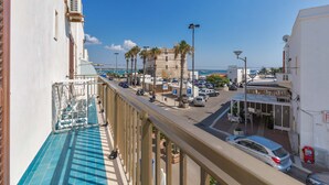 A balcony with a pool, overlooking a street with parked cars and palm trees.