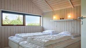 Een slaapkamer met houten wanden, een groot raam en een bed met witte beddengoed.
