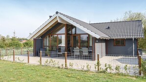 Een modern huis met een schuin dak, grote ramen en een omheinde tuin.