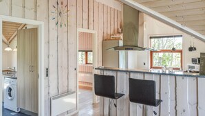 Een keuken met houten wanden, een inbouwfornuis, een raam en een wasmachine in de aangrenzende ruimte.