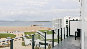 Ein modernes Gebäude mit einem Balkon mit Blick auf einen Strand, einen Leuchtturm und ein ruhiges Meer.