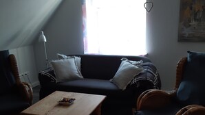 A living room with a dark-colored sofa, two wicker armchairs, a wooden coffee table, and a floor lamp. - Vacation with a dog in North Frisia (Klanxbüll)