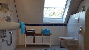 A compact bathroom with a skylight, a sink, a toilet, and a small storage unit with towels. - Vacation with a dog in North Frisia (Klanxbüll)