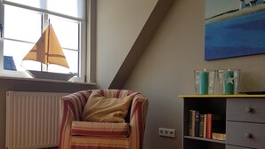 A cozy room with a striped armchair, a bookshelf, and a painting of a lighthouse. - Vacation with a dog in North Frisia (Klanxbüll)