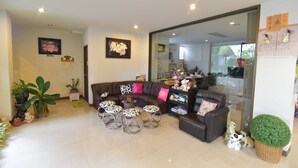A modern living room with a brown leather sofa, a glass coffee table, and a dining area visible through a glass door. - Kyongean Mansion 2 (Krabi)