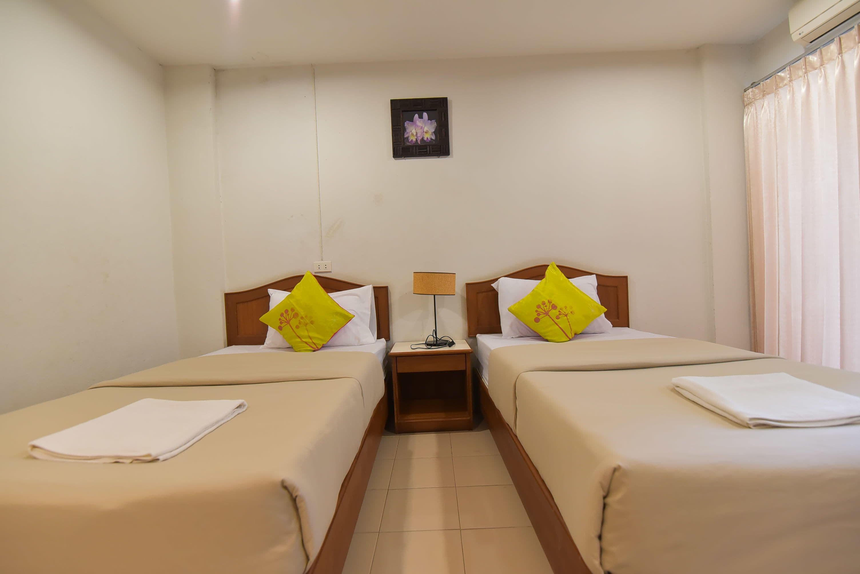 Una habitación de hotel con dos camas, cada una con una almohada y una mesita entre ellas.