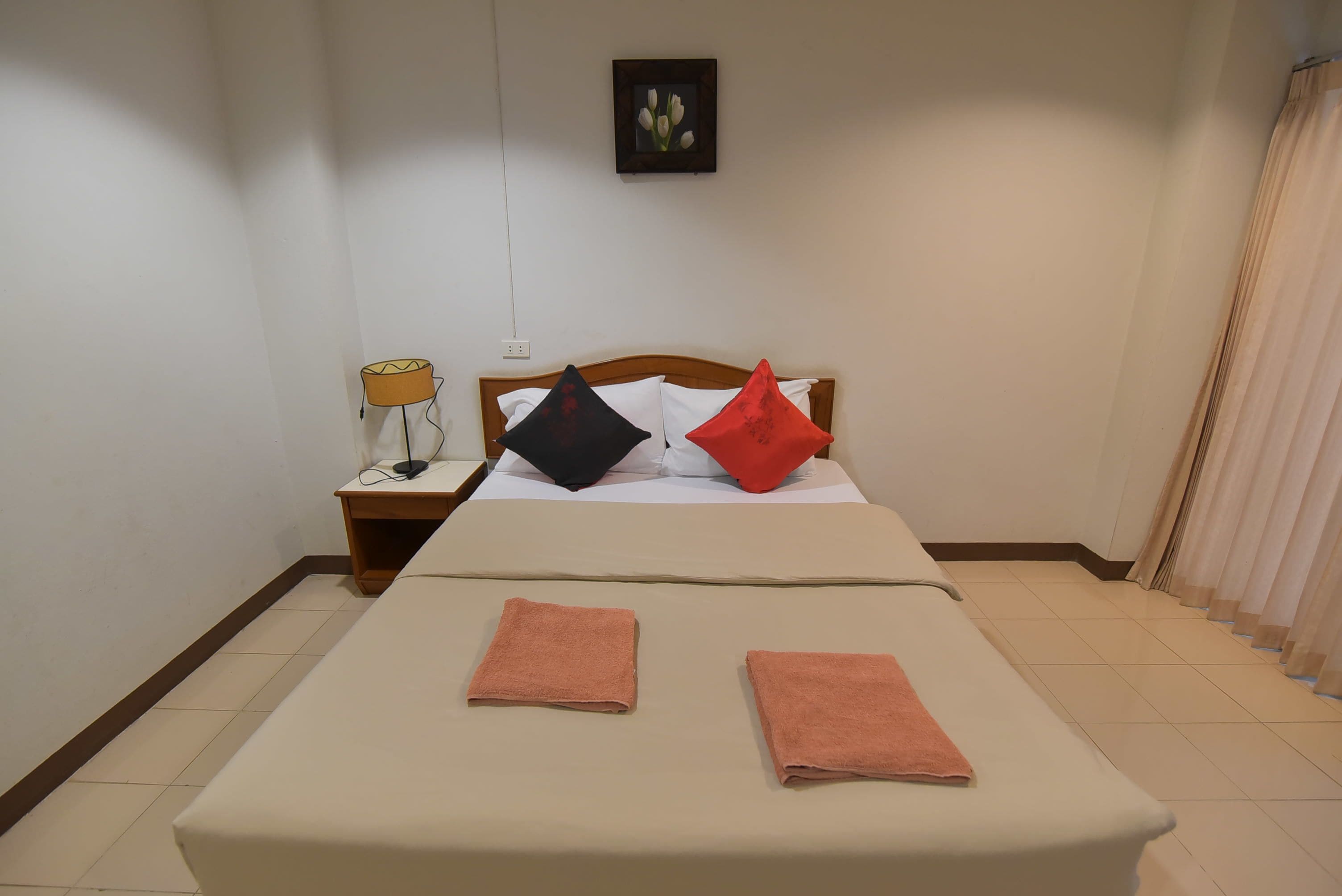 A neatly made bed with two towels, a bedside lamp, and a picture on the wall.