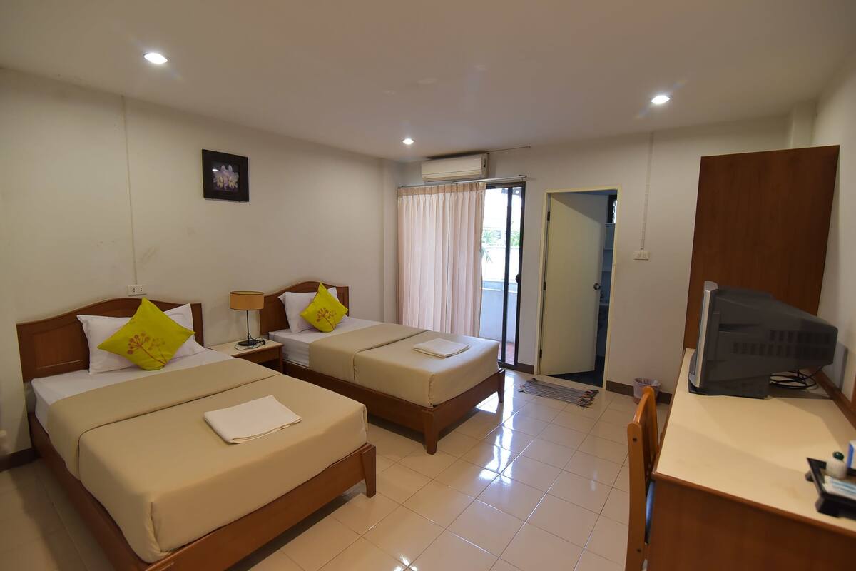 A hotel room with two beds, a desk with a computer, and a sliding door leading to a balcony.