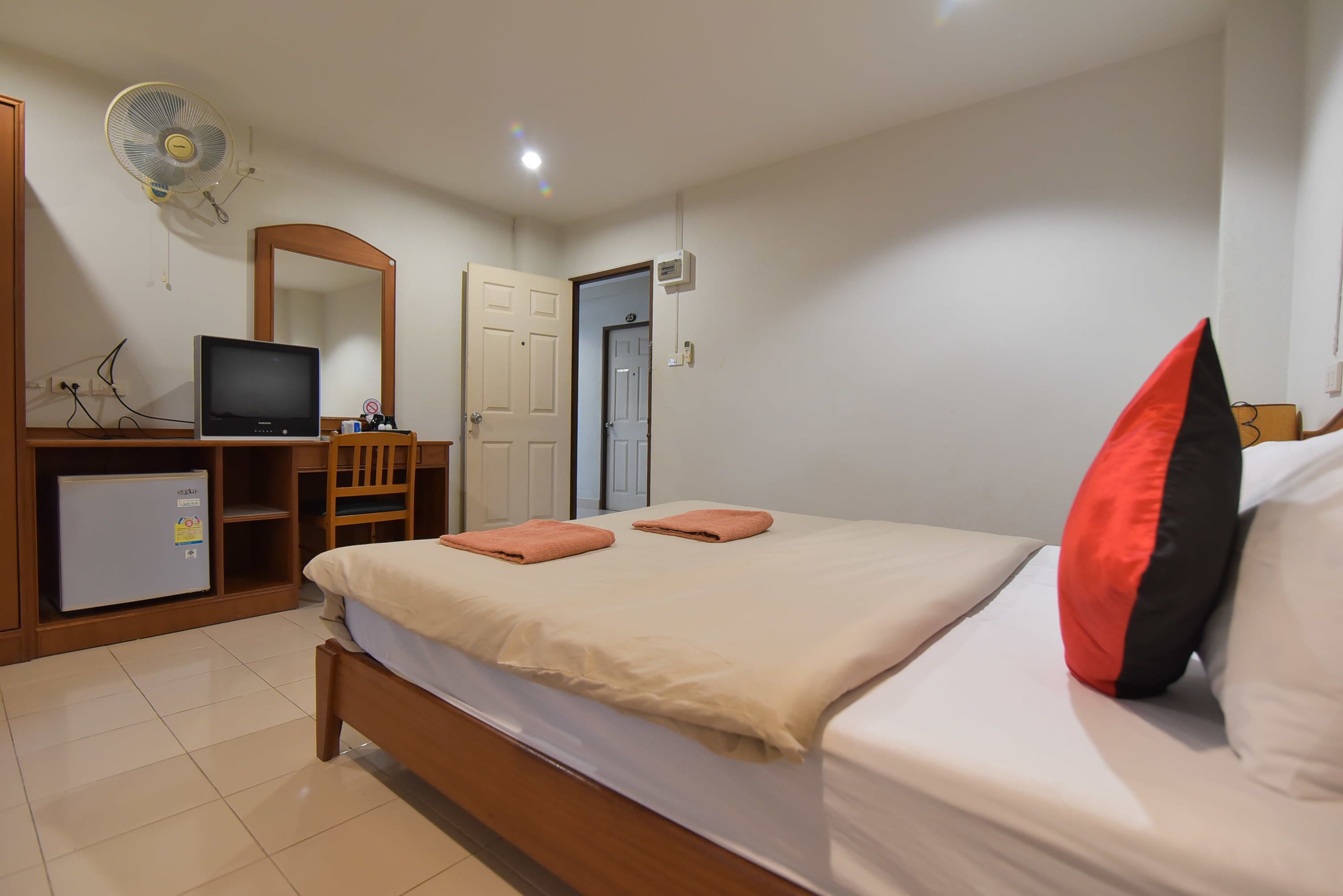 A hotel room with a bed, a desk with a computer, a small fridge, a mirror, and a door.
