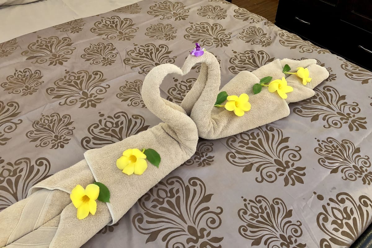 Una cama con una colcha estampada y dos toallas dispuestas en forma de cisne, cada una con una flor amarilla.