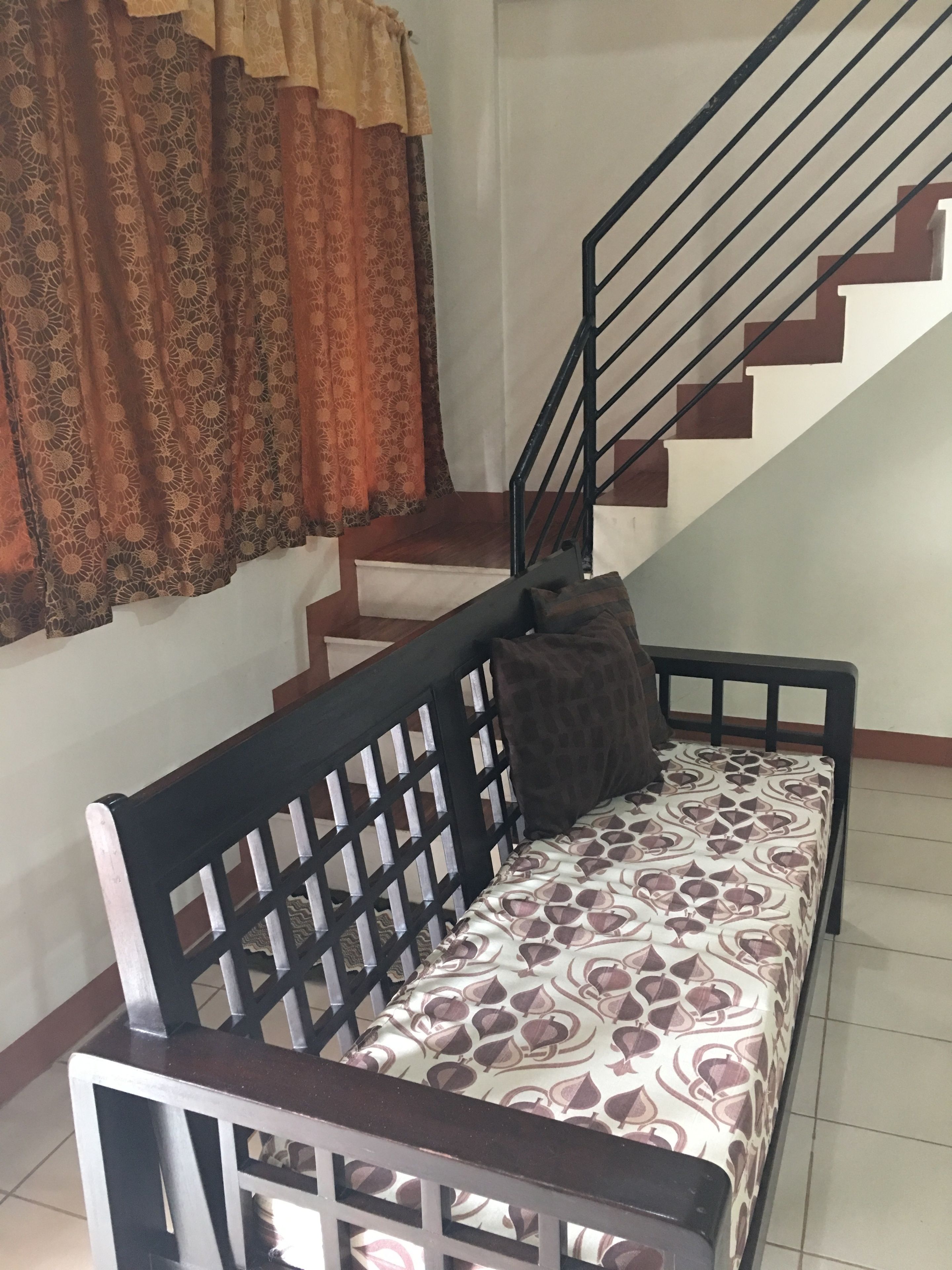 A staircase with a black railing, a patterned sofa with a cushion, and a window with patterned curtains.