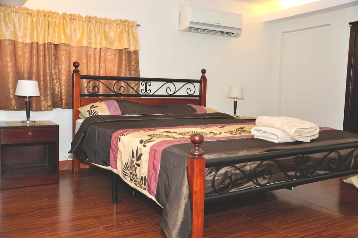 Una cama bien hecha con cabecera de madera, una mesita de noche con lámpara y un aire acondicionado instalado en la pared.