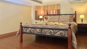 Una cama bien hecha con una toalla dispuesta en forma de corazón, una lámpara de noche y un aire acondicionado de pared.