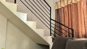 Una escalera con barandillas negras, una pared color crema y una ventana con cortinas estampadas.