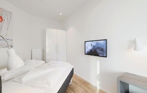 A modern bedroom with a bed, a wardrobe, a TV mounted on the wall, and a bedside table.