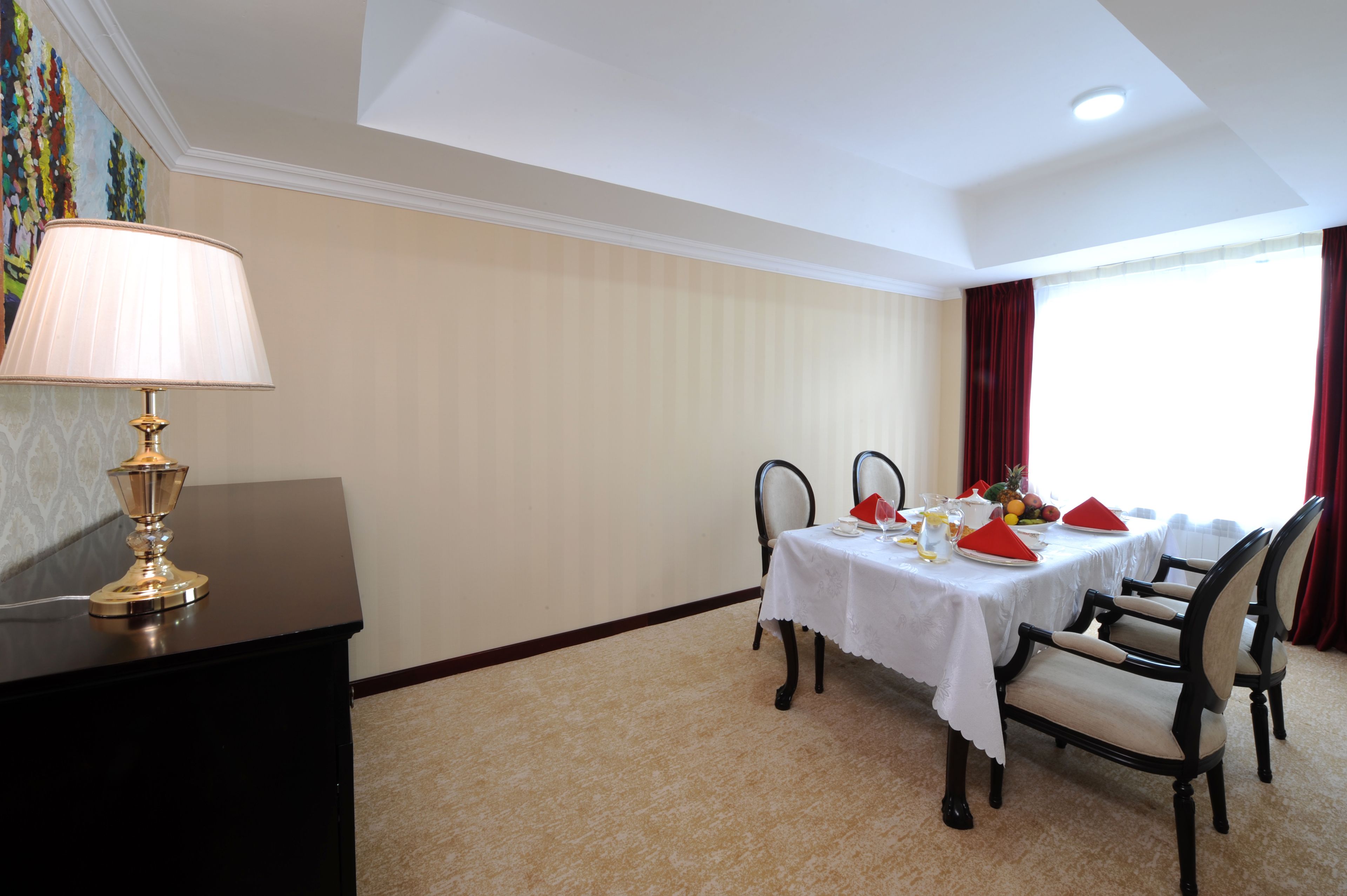 Un comedor con una mesa preparada para cuatro personas, una lámpara y un cuadro en la pared.
