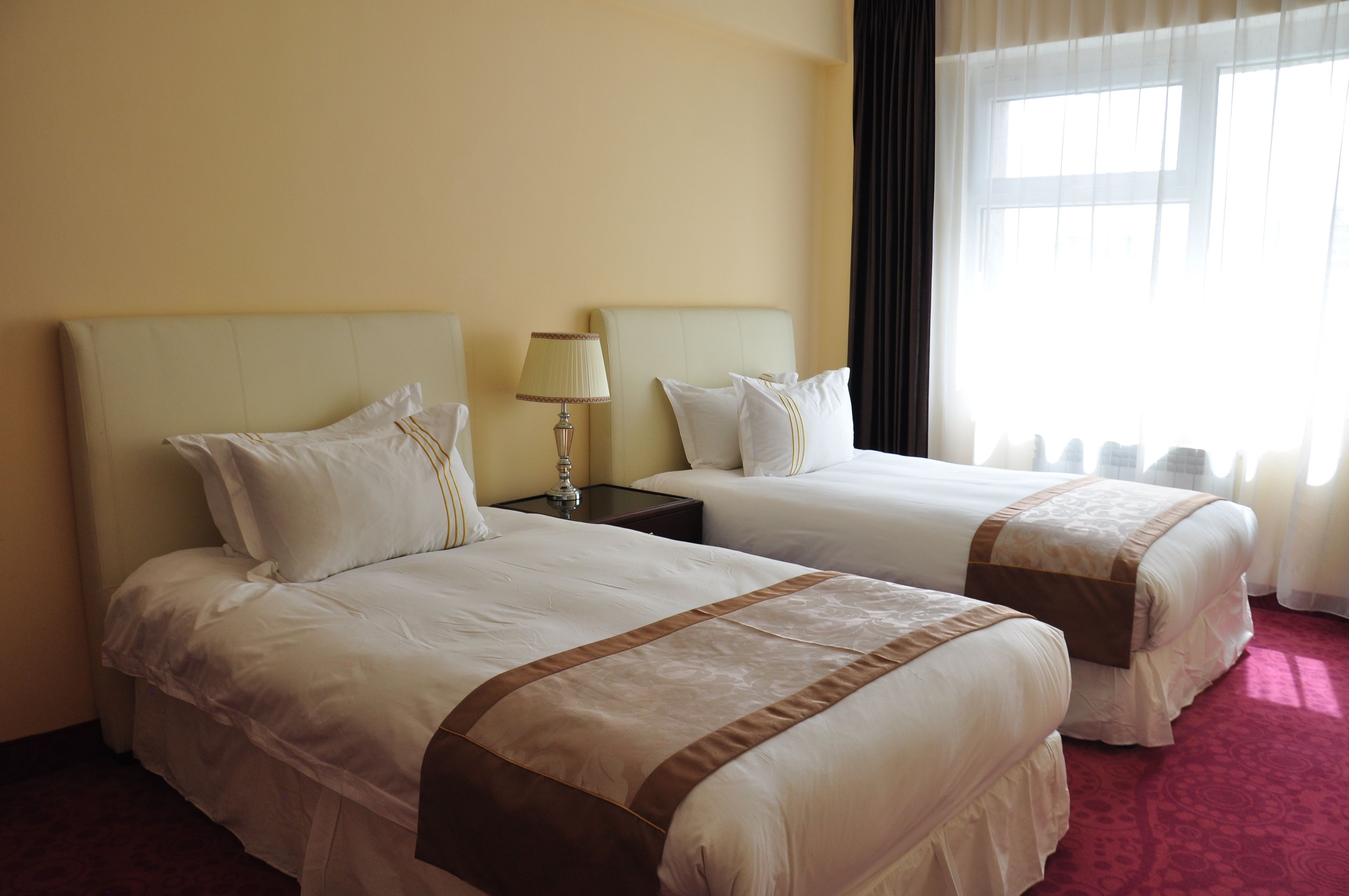 Una habitación de hotel con dos camas, una mesita de noche con lámpara y un ventanal con cortinas.