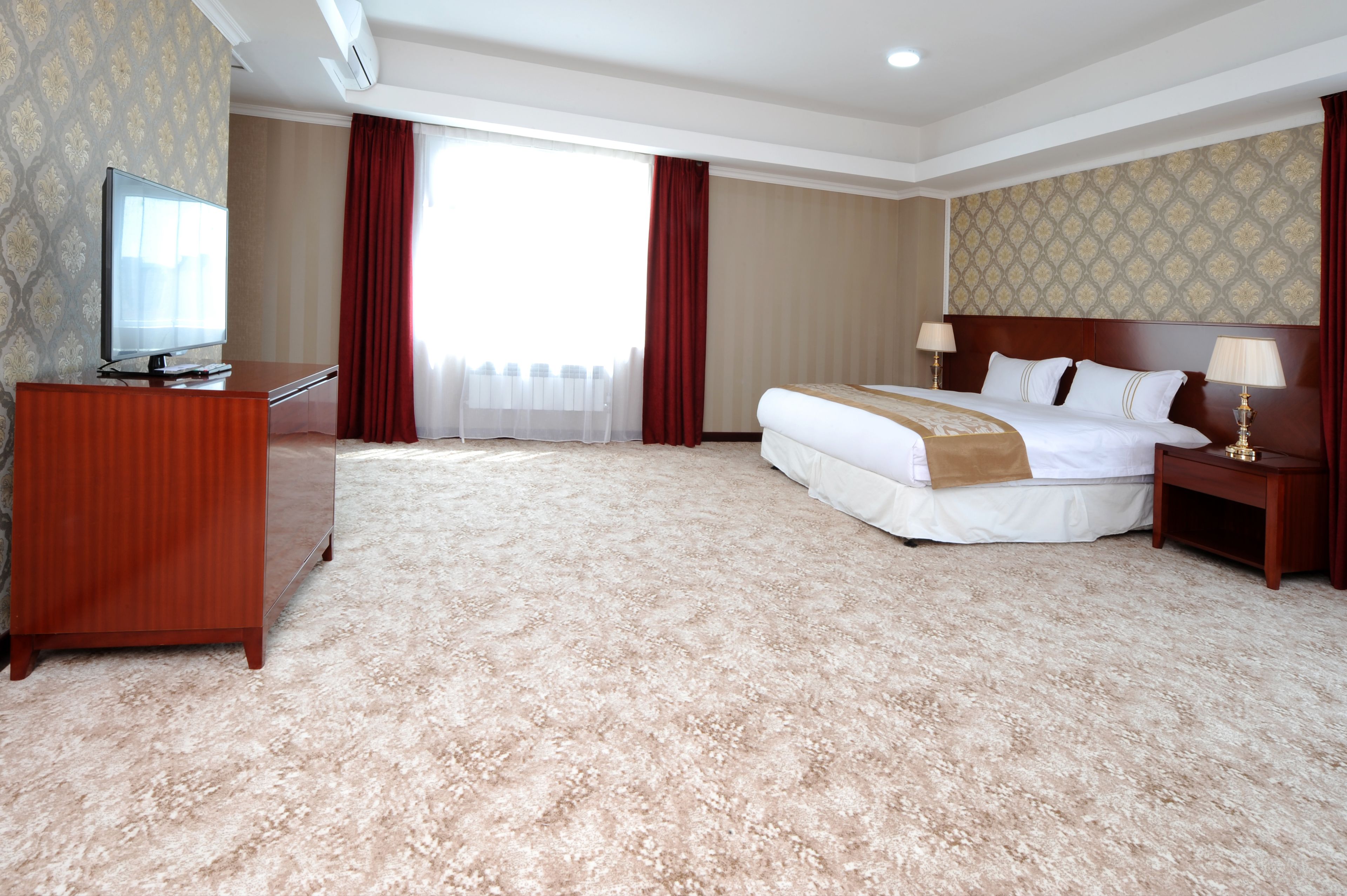 A hotel room with a large bed, a TV, a desk, and a carpeted floor.