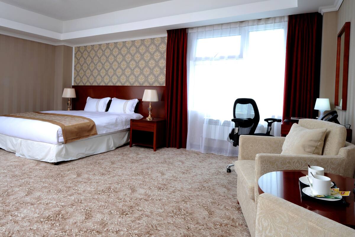 A hotel room with a large bed, a sofa, a desk with a chair, and a window with curtains.