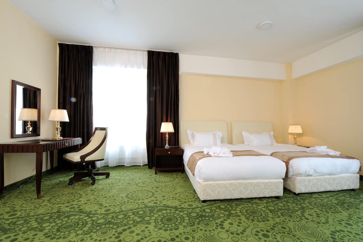 A hotel room with two beds, a desk, a chair, and a large window with curtains.