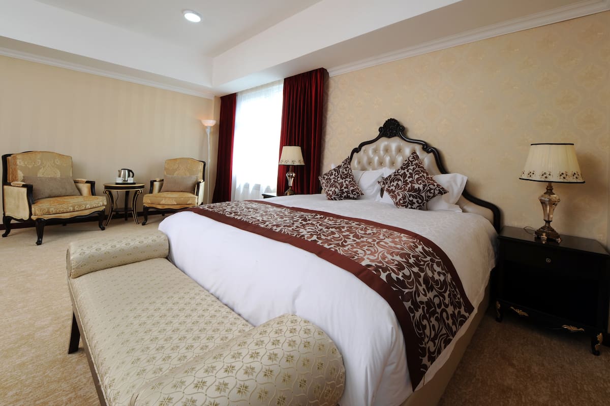 A hotel room with a large bed, two armchairs, a small table with a lamp, and a bench.