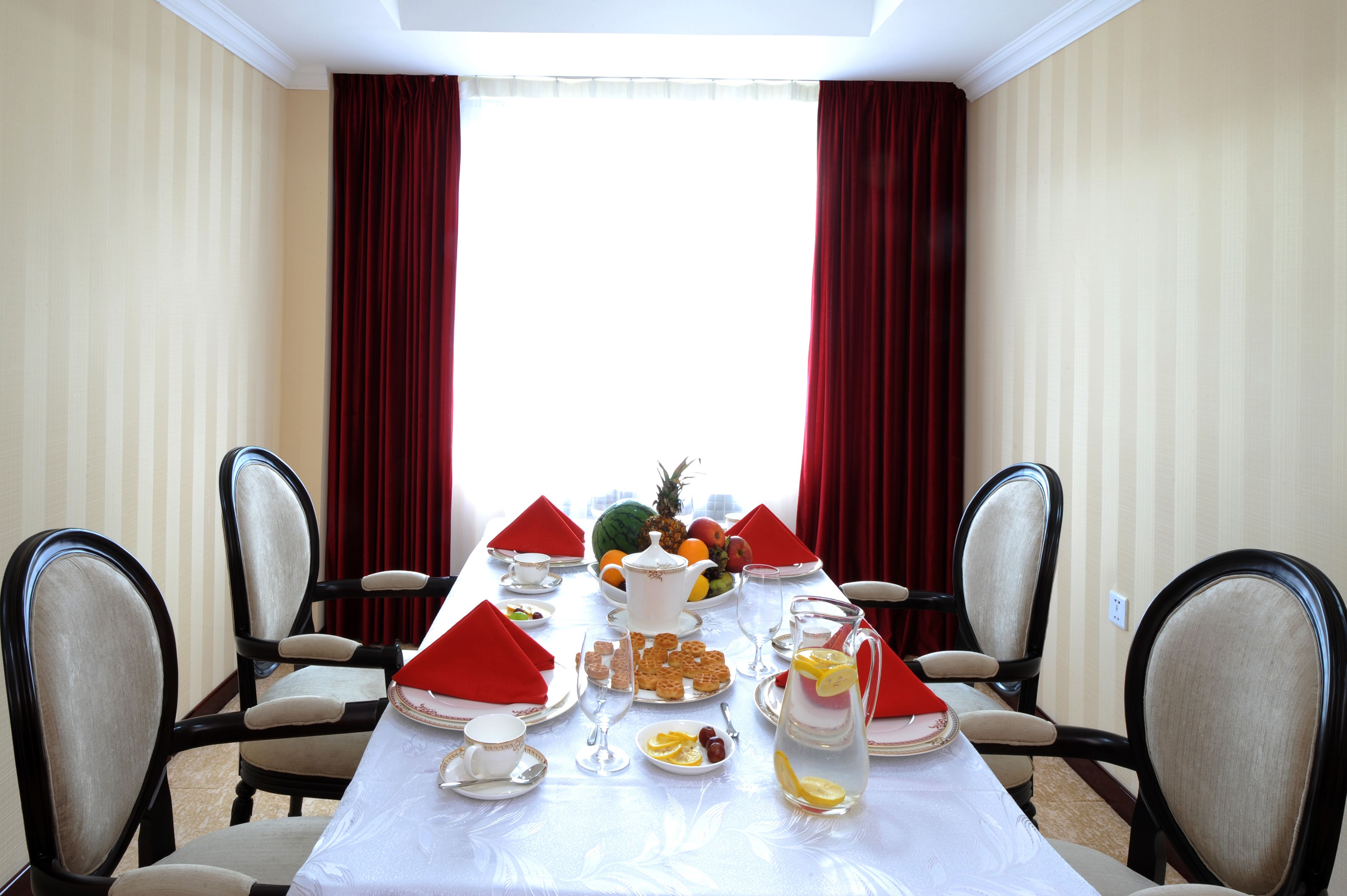 A dining table set for six with red napkins, plates, and glasses, surrounded by chairs.