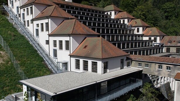 Un hôtel moderne composé de plusieurs bâtiments blancs, chacun coiffé d’un toit brun, situé sur une colline.