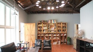 Una habitación amplia con suelo de madera, una gran estantería llena de libros, sillones de cuero, una mesa de madera y una ventana que deja entrar luz natural.