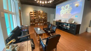 Una biblioteca con pisos de madera, mobiliario de cuero y una pantalla grande que muestra '20th Century Fox'.