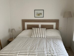Ein Bett mit gestreifter Bettdecke, einem Kopfteil, einer Nachttischlampe und einem gerahmten Bild an der Wand.