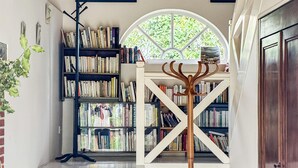 A library with bookshelves, a wooden coat rack, and a large arched window. - Cozy home in Beauchene with WiFi (Beauchene)