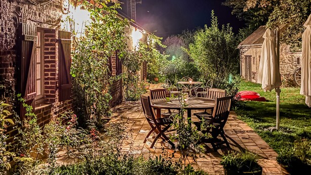 A patio with a table and chairs, surrounded by greenery and a stone wall. - Cozy home in Beauchene with WiFi (Beauchene)